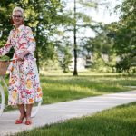 Senior woman smiling with her bicycle on a sunny path, enjoying the outdoors.